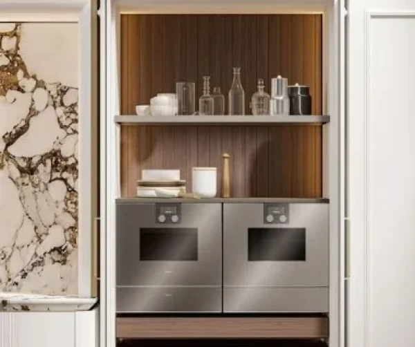 Integrated wine bar and storage cabinet featuring a wine rack, glass holders, dark wood drawers, and a wine cooler, framed by white paneled cabinetry and two fluted glass display cabinets.