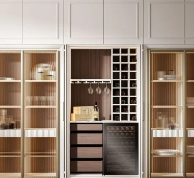 Integrated wine bar and storage cabinet featuring a wine rack, glass holders, dark wood drawers, and a wine cooler, framed by white paneled cabinetry and two fluted glass display cabinets.