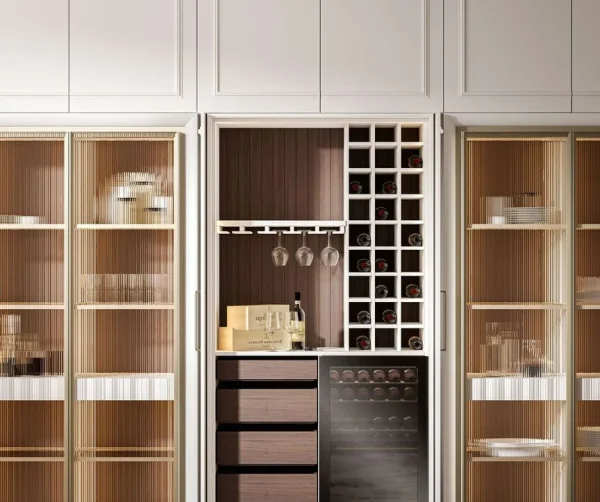 Integrated wine bar and storage cabinet featuring a wine rack, glass holders, dark wood drawers, and a wine cooler, framed by white paneled cabinetry and two fluted glass display cabinets.